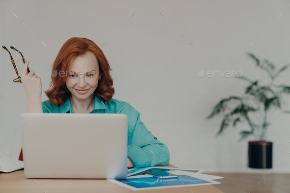 Happy beautiful female financial analyst prepares economic research, works on laptop.