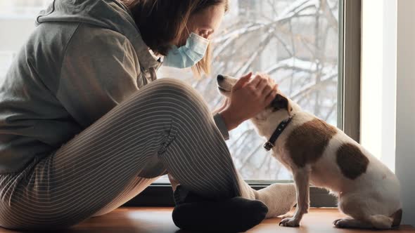 Woman Sitting in Mask at Window with a Dog alt