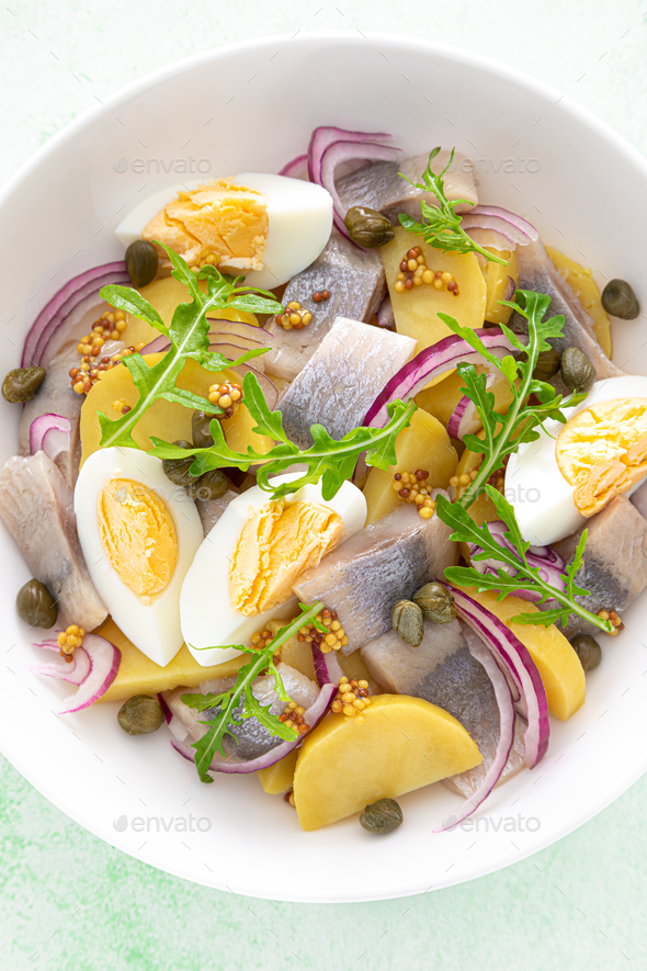 Herring and boiled potato salad with egg, capers and red onion. Top view Stock Photo by sea_wave