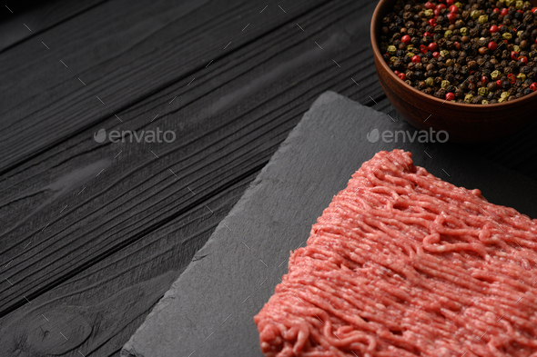 Mix of different types of pepper and minced meat on a black rustic background. P