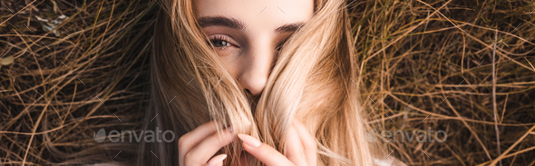 horizontal image of sensual blonde woman lying on green grass and obscuring face with hair, top view