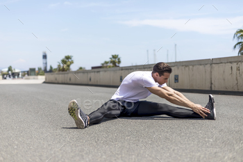 Portrait of sitting runner outside doing stretch in street