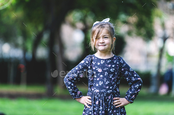 Front view of happy little girl in dress standing in the park
