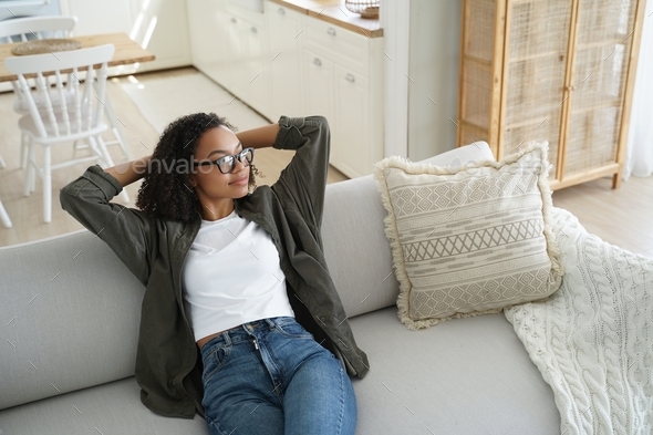 Calm african american young girl sitting relaxing dreaming on cozy couch in living room at home