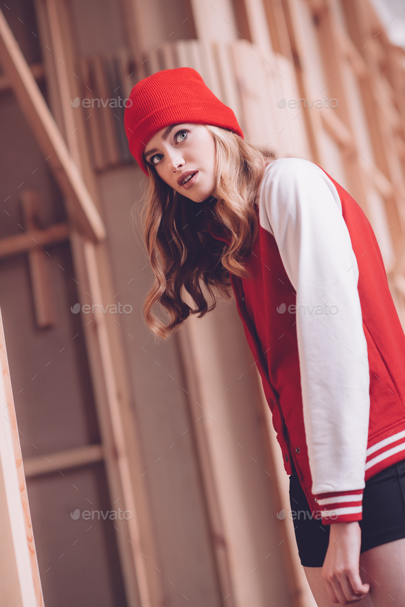 Stylish hipster woman in baseball jacket and red hat posing
