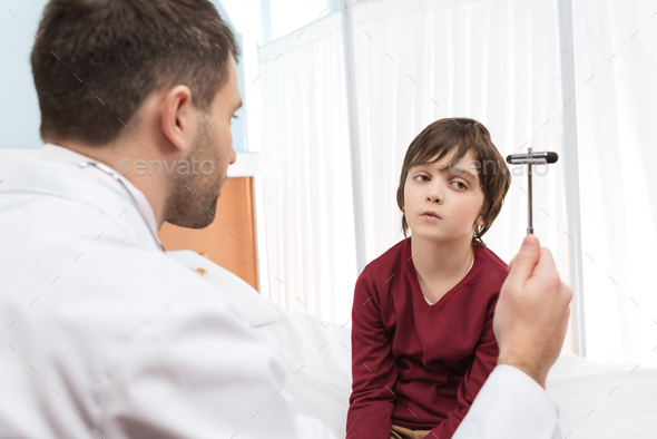 Bored little boy looking at man doctor with reflex hammer