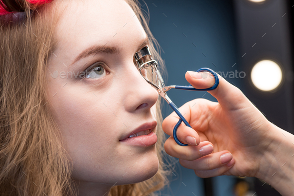Close-up view of makeup artist correcting eyelashes with curling tongs of beautiful young woman