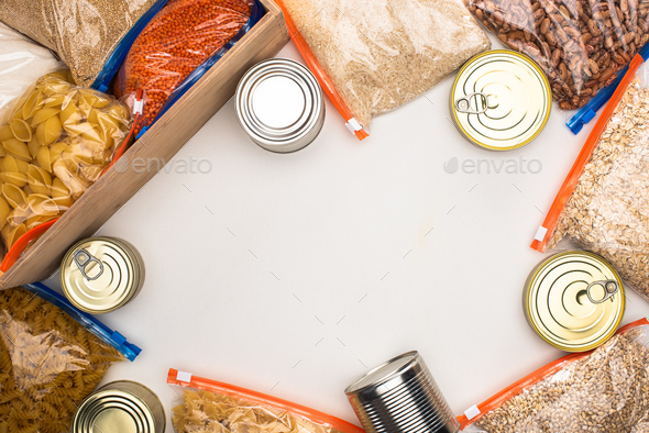 top view of cans and groats in zipper bags with wooden box on white background, food donation