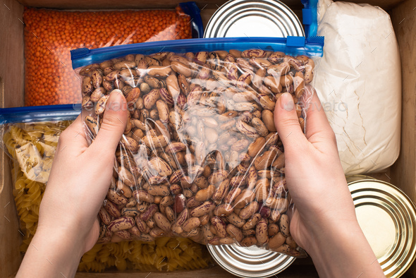cropped view of woman holding beans in zipper bag, food donation concept