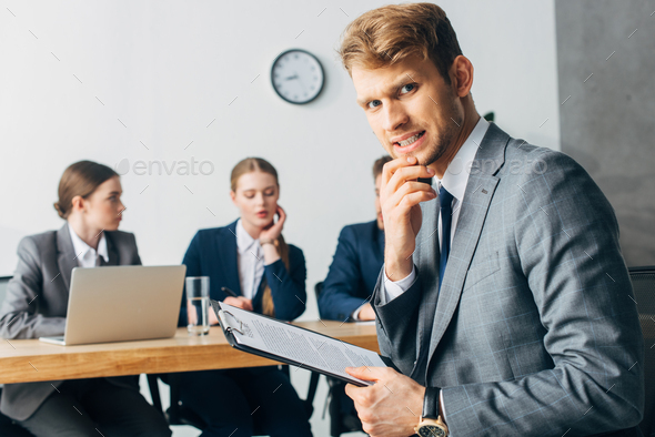 Selective focus of scared employee with resume looking at camera near recruiters in office