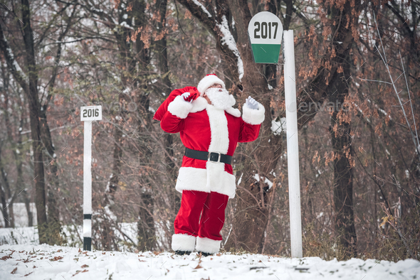 Santa Claus walking on snowy road with red sack full of gifts on back