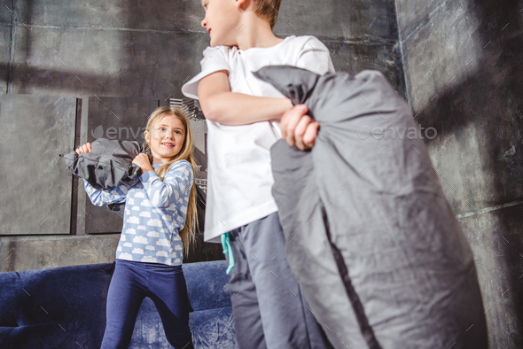 Cute happy siblings fighting with pillows in bedroom