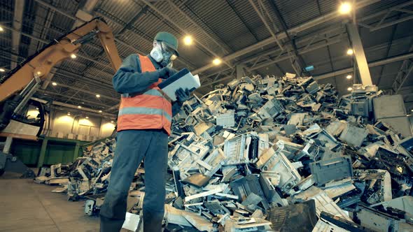 Discarded Electronics and a Landfill Worker Inspecting It alt