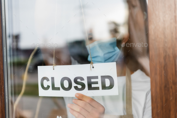 waiter in medical mask hanging card with closed lettering on cafe entrance door