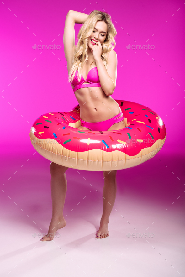 Beautiful blonde young woman in swimsuit posing with swimming tube in shape of doughnut