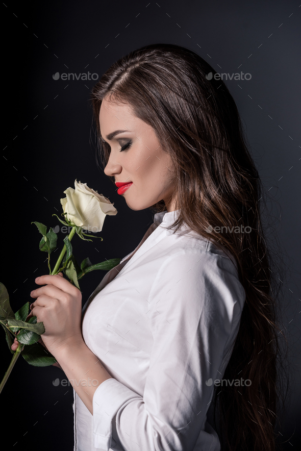 young woman smelling white rose with eyes closed isolated on black
