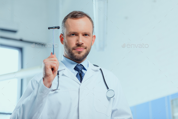 portrait of confident doctor with stethoscope holding reflex hammer