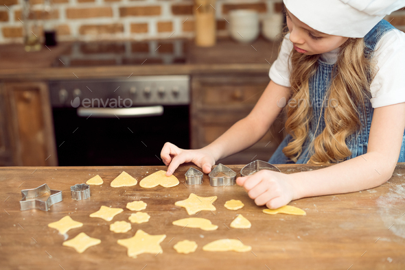side view of little girl in chef hat making shaped cookies in kitchen - Stock Photo - Images