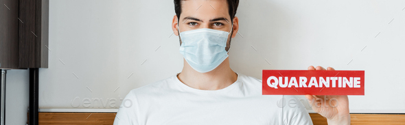 Man in medical mask holding card with quarantine lettering at home, panoramic crop