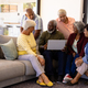 Multiracial senior man holding laptop explaining to friends while sitting on sofa in nursing home - PhotoDune Item for Sale