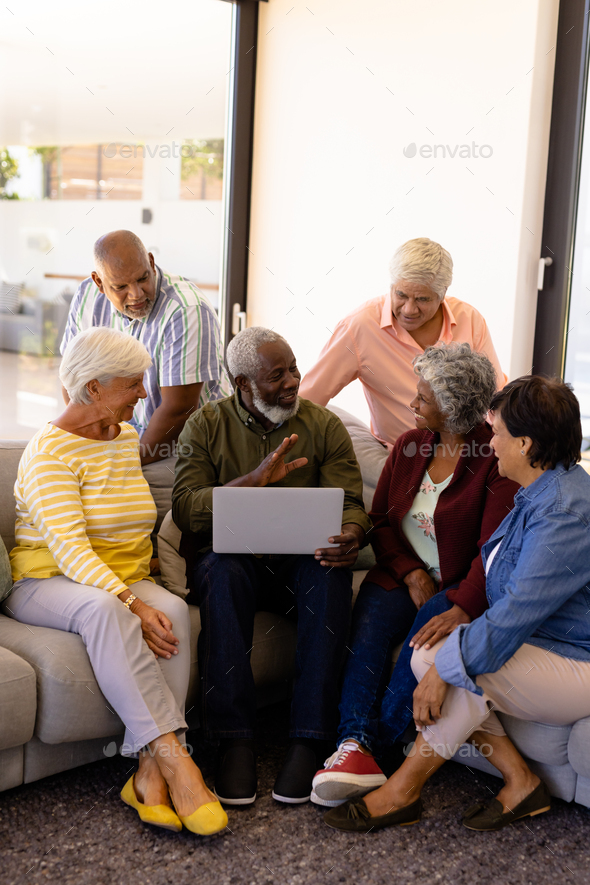 Multiracial senior man holding laptop talking with friends while sitting on sofa in nursing home - Stock Photo - Images
