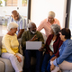 Multiracial senior man holding laptop talking with friends while sitting on sofa in nursing home - PhotoDune Item for Sale