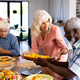 Multiracial senior woman serving food to male friend at dining table in nursing home - PhotoDune Item for Sale