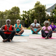 Multiracial senior friends meditating on mats while sitting on hardwood floor against plants in yard - PhotoDune Item for Sale
