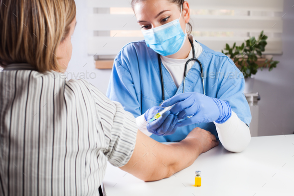 Young female doctor vaccinating elderly patient in UK GP's office - Stock Photo - Images