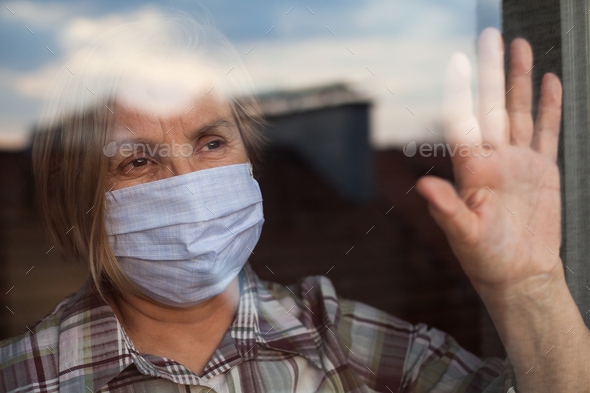 Portrait of elderly senior citizen wearing face mask looking through room window - Stock Photo - Images
