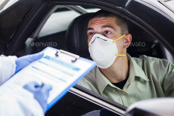Driver wearing protective N95 face mask sitting by left drive wheel in UK drive-thru test centre - Stock Photo - Images