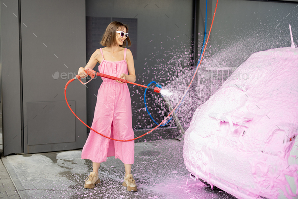 Woman in pink dress washing her tiny car with nano foam at car wash