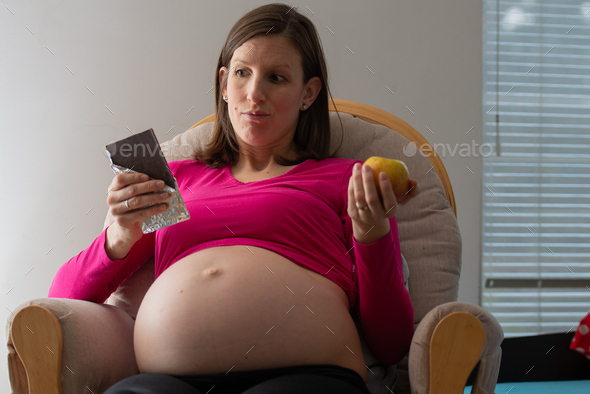 Pregnant woman deciding between a a healthy choice of an apple and an unhealthy chocolate
