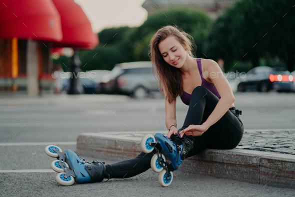 Woman puts on rollerskates going to ride rolles in urban place has regular exercising.