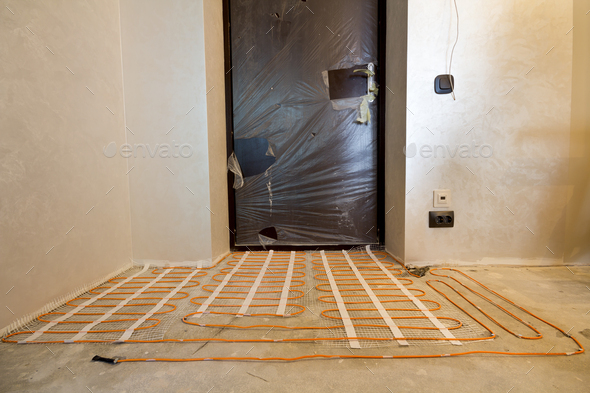 Heating red electrical cable wire system installed on cement floor in small new unfinished room with