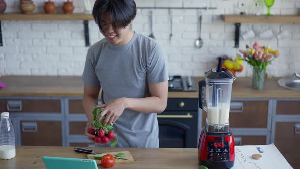 Cheerful Asian Man with Toothy Smile Cooking Healthful Salad and Talking at Tablet Web Camera alt