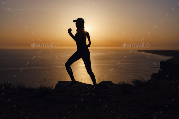 Side view of fitness woman running on a road by the sea.