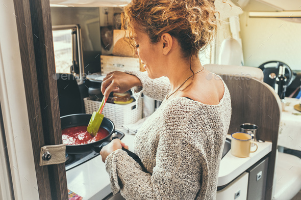 Woman viewed from back preparing and cooking tomato sauce for lunch inside a modern van