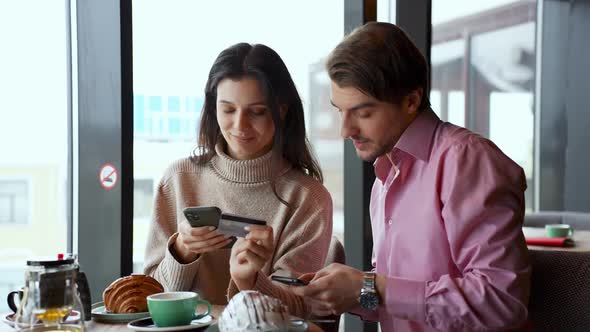 A Young Couple Enters Credit Card Details and Makes a Purchase Via the Internet in a Cafe