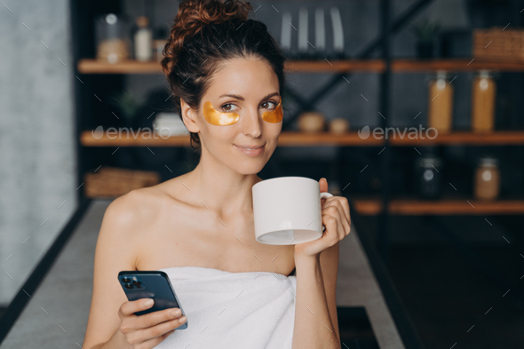 European girl drinks coffee and texting on smartphone and relaxing. Evening body care routine.