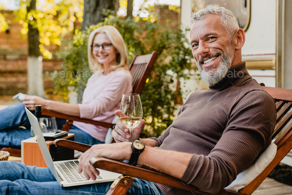 Successful elderly married couple resting on the deck chairs on the porch of their camper