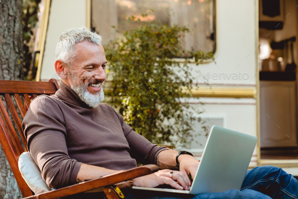 Close up portrait of a cheerful senior male traveler working on his laptop in deck chair