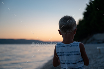 Toddler boy standing on the beach in the evening