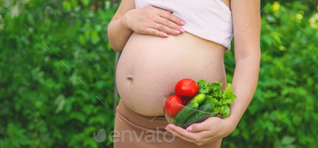 A pregnant woman with vegetables in her hands. Selective focus.