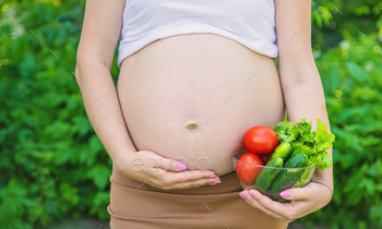 A pregnant woman with vegetables in her hands. Selective focus.