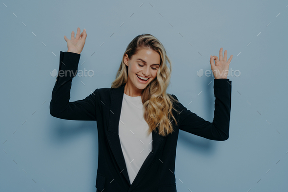 Happy woman with blonde dyed hair raising her arms and dancing with closed eyes