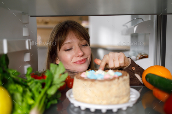 Girl tasting cake with finger in fridge