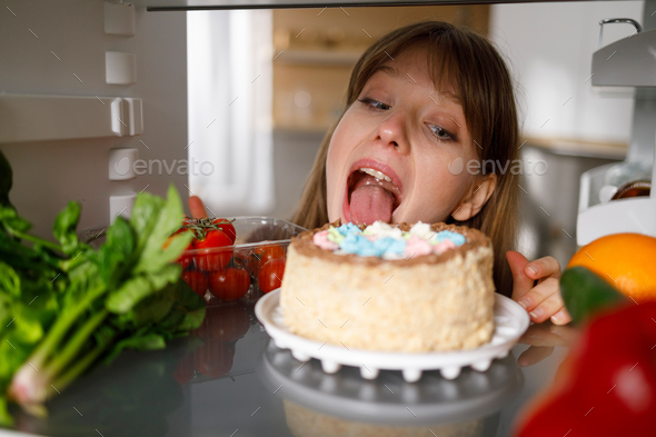 Woman licking a cake in the fridge