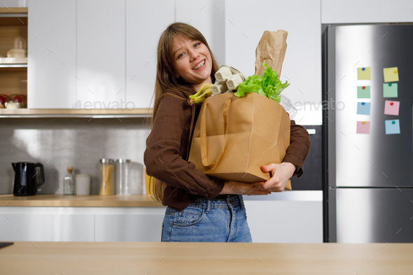 Cheerful woman in the kitchen with a heavy shopping bag full of groceries