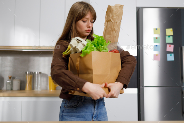 Young woman holds in her hands a heavy paper shopping bag full of fresh vegetables and products.